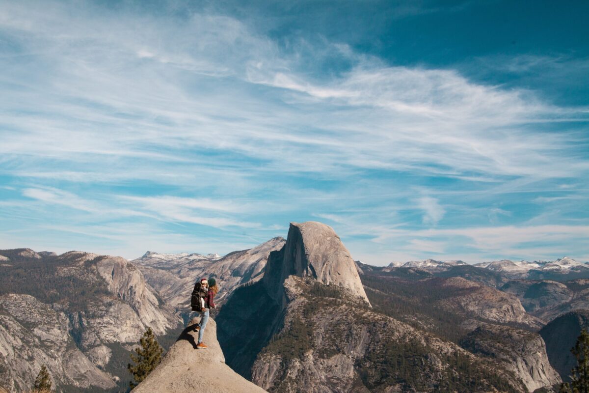 Woman hiking with baby in hiking carrier looking out at half dome in yosemite.