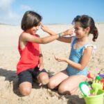 two children on the beach put sunscreen on eachother's faces