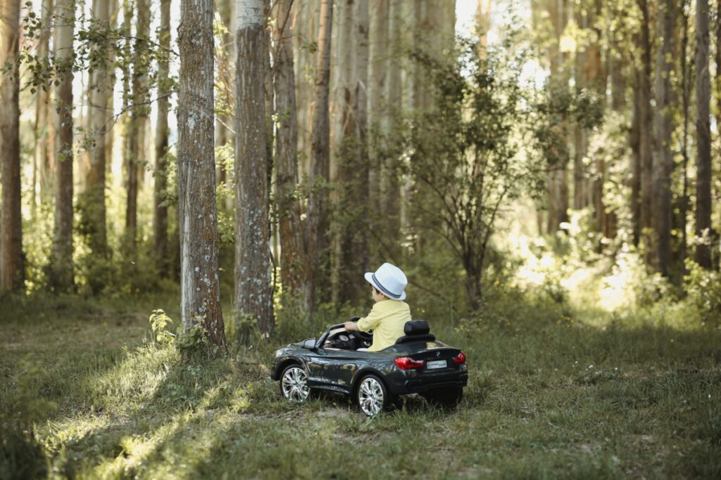 child in a hat rides in a toy car through a grove of trees