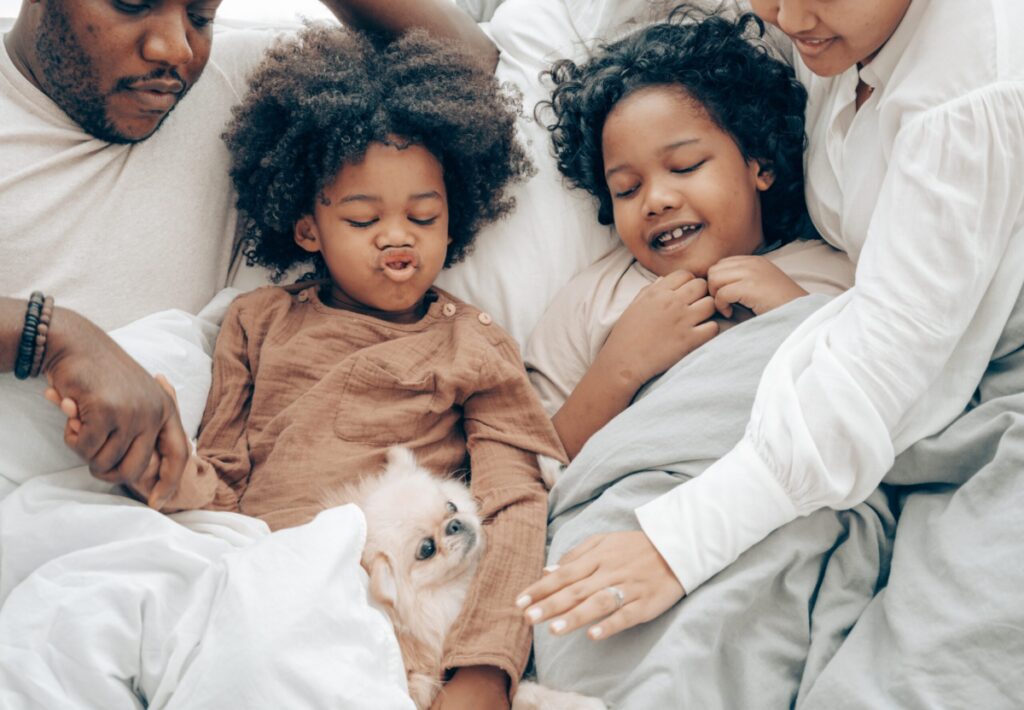Family relaxing in bed with small dog
